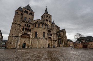 Fototapeta na wymiar Trier / Germany - February 9 / 2019 : front view of Saint Peter's cathedral at a cloudy day and a tree at side of it