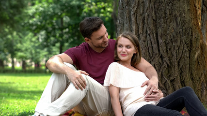 Fototapeta na wymiar Happy pregnant couple sitting in park, planning secured family life, welfare