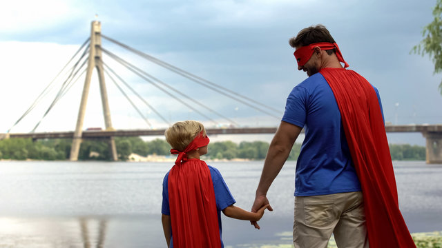 Dad and son in superhero costumes holding hands, father protection and support