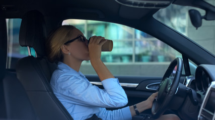 Fototapeta na wymiar Businesswoman drinking coffee while driving car, lack of sleep, busy lifestyle