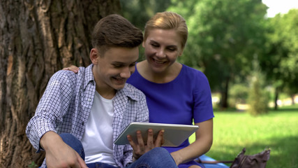 Mom and son watching funny video on tablet, surfing net in park, time together