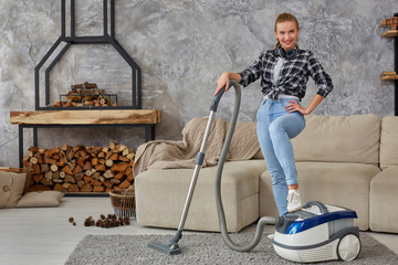 Young smiling woman vacuum cleaning the carpet in the living room, modern scandinavian interior....