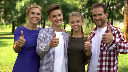 Joyful family members enjoying weekend in park and showing thumbs up into camera