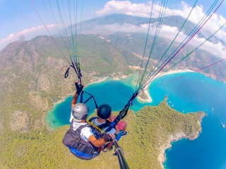 Paragliding in the sky. Paraglider tandem flying over the sea with blue water and mountains in...