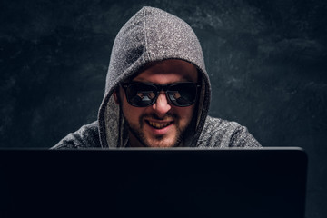 Portrait of a bearded satisfied hacker with a laptop on a black background