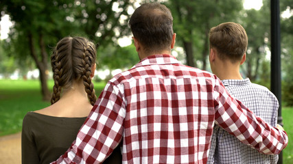 Adult father walking with daughter and son in park, hugging and talking, family