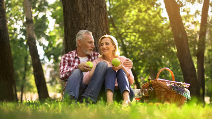 Family weekend, retired couple sitting in park and eating green apples, picnic