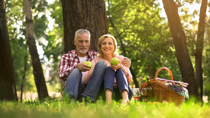 Fototapeta na wymiar Senior couple sitting in park and eating green apples, picnic, family weekend