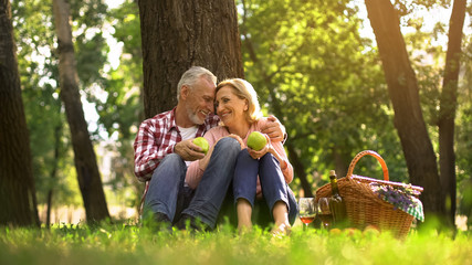 Loving old couple hugging in park and eating green apples, picnic family weekend