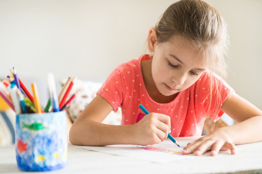 Little preschooler girl diligently drawing something with blue pencil