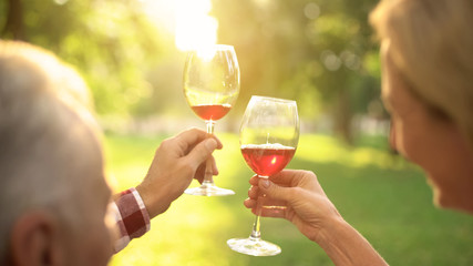 Senior couple holding wineglasses and drinking alcohol beverage on outdoor date