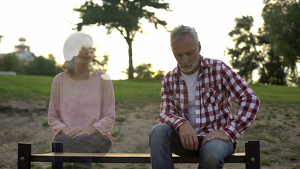 Depressed old man sitting on bench, wife appearing beside, loss sorrow, memories