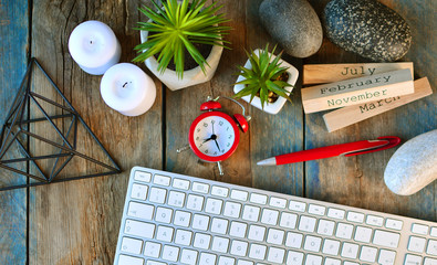 Creative desktop mess of creative person. Clock, computer keyboard, pen, flowers, prism figure, candles, stones and calendar on a wooden table.