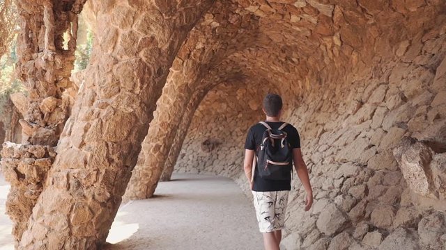 Young man is viewing amazing artificial cave, touching stones in wall, back view