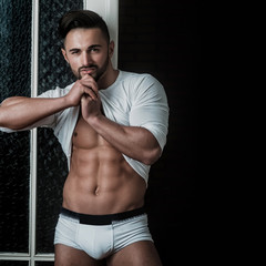 Strong athletic sexy muscular male model wearing white sweater on black background. Seductive...
