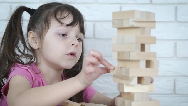 Wooden blocks are falling. Cute little girl is playing balance game.