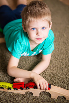 happy baby, blonde with blue eyes, a little boy of five years in the mint (green / blue) t-shirt in shorts barefoot near the couch in the apartment igret fun with wooden railway