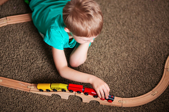 happy baby, blonde with blue eyes, a little boy of five years in the mint (green / blue) t-shirt in shorts barefoot near the couch in the apartment igret fun with wooden railway