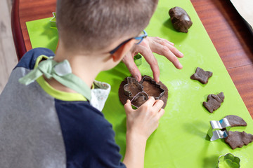 Przygotowywanie cynamonowych ciasteczek. Chłopiec układa metalowe foremki na rozwałkowanym kawałku ciasta. - obrazy, fototapety, plakaty
