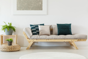 Green plant grey pot on wooden stand next to scandinavian couch with pillows and beige futon
