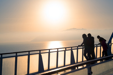 Silhouette of travelers on board watching coastline in mist at sunrise