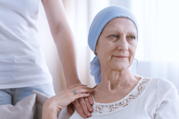 Daughter supporting senior woman wearing blue headscarf, suffering from lung cancer