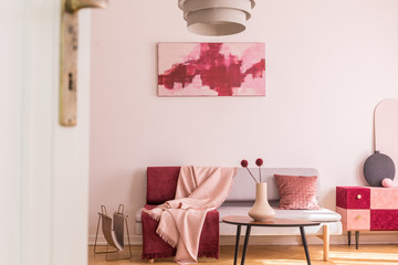Abstract burgundy and pastel pink painting on empty white wall of trendy living room interior with grey sofa and cabinet