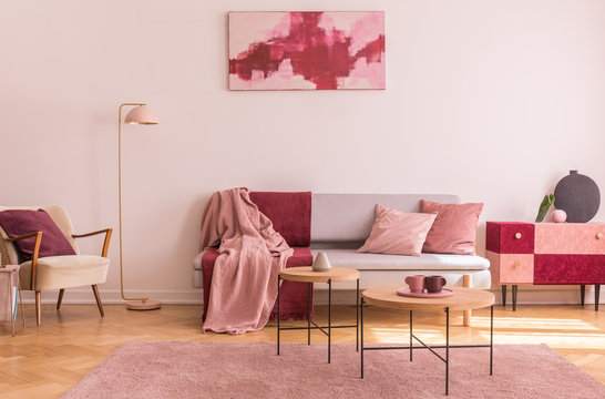 Abstract burgundy and pastel pink painting on empty white wall of fashionable living room interior with classy armchair and fashionable sofa