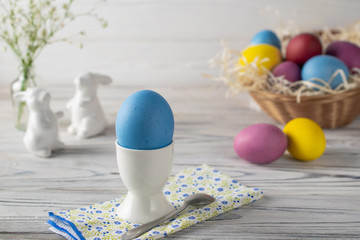Happy easter table setting with dyed blue egg in egg cup and basket with colorful eggs