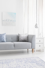 Grey sofa with cushions near lamp in minimal living room interior with poster and carpet. Real photo