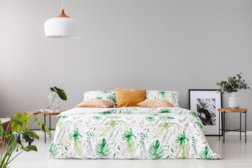 Double bed with floral duvet and peach colored pillow between two wooden nightstands with flowers in vases on it