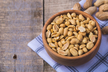 Peanuts in small wooden bowl on natural rustic desk.