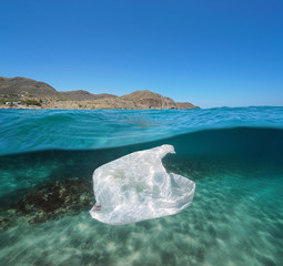 Pollution underwater sea a plastic bag adrift in the Mediterranean with the coast in background, split view half above and below water surface, Spain