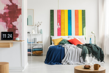 Modern, open space apartment interior with a home office in the foreground and a bedroom with a colorful bedhead in the background. Real photo