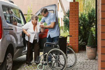 Senior woman getting out of the car with the help of a nurse