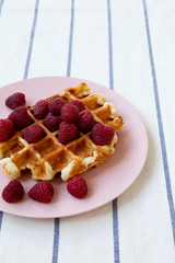 Traditional belgian waffle with raspberries on pink plate, side view. Close-up.