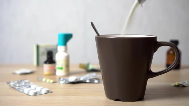 Hand pours and stirs the medicine in a mug against a bunch of pills on the table 4K