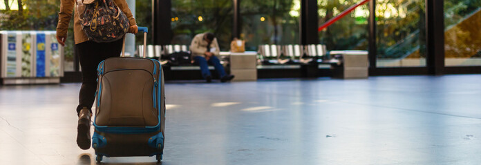Obraz premium Young woman sitting in the terminal waiting room and waiting for departure, she is texting and connecting with her smartphone