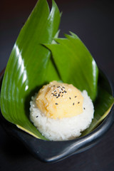 Riz gluant au lait de coco sucré, pâte de soja et graines de sésame noir sur feuille de bananier