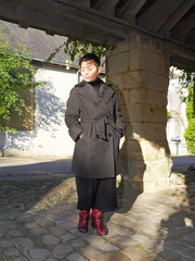 Femme manteau gris et bottes rouge sous un préau ancien