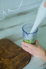 Female hands making Green smoothie of celery and banana with white immersion blender and measuring...