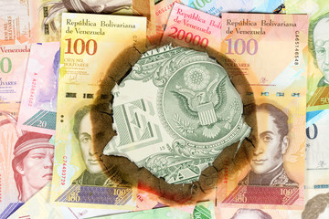 Venezuela hyperinflation concept. Burned Venezuelan banknotes of different bolivar value, through the hole in which you can see the unburned one dollar bill reverse side. Close up