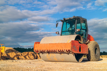 Compactor in the sunset prepares the grounf for making the road