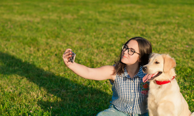 Pretty young woman with friendly golden retriever dog taking a selfie with a smartphone. Beautiful girl and her dog make self-portrait themselves by phone