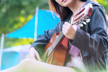 Travel alone young woman playing acoustic guitar at camping. Girl playing guitar in her free time hand focus.