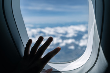 View from airplane window. Aerial landscape. Flying over clouds. Hand touching the glass