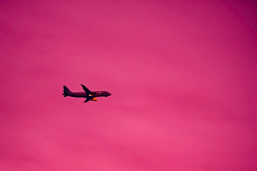 Fototapeta na wymiar Silhouette of passenger plane crossing the sky, copy space pink background.