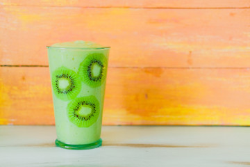 Green smoothie of celery and banana in glass decorated with slices of kiwi on wooden orange background. Healthy vegan lifestyle