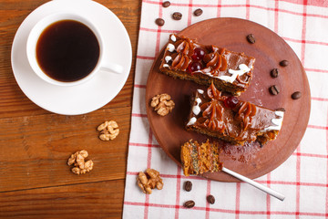 a piece of cake with caramel cream  on a wooden kitchen board and a cup of coffee, brown wooden background..