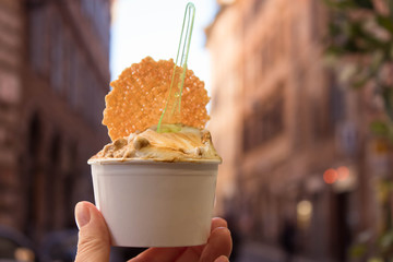 hand with ice cream on the Roman street background.  Italian traditional ice cream gelato 